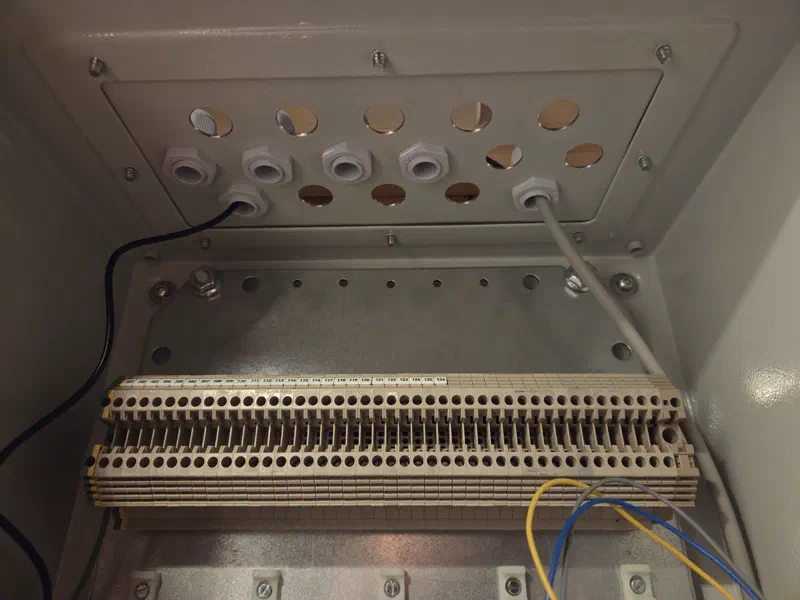 Holes, cable glands, and terminal blocks at the top of the alarm cabinet